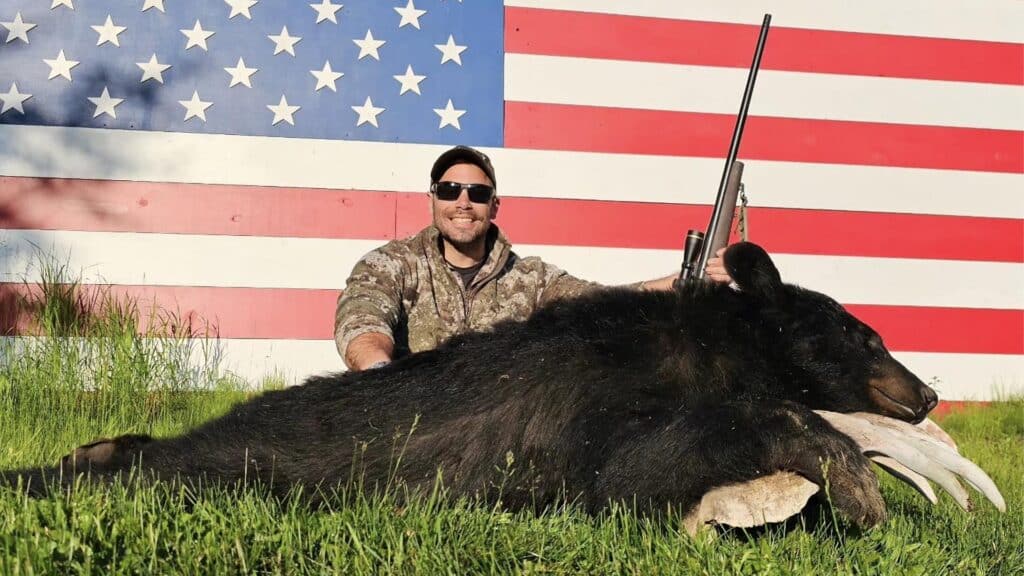 hunter holding rifle showing his bear in front of the American Flag